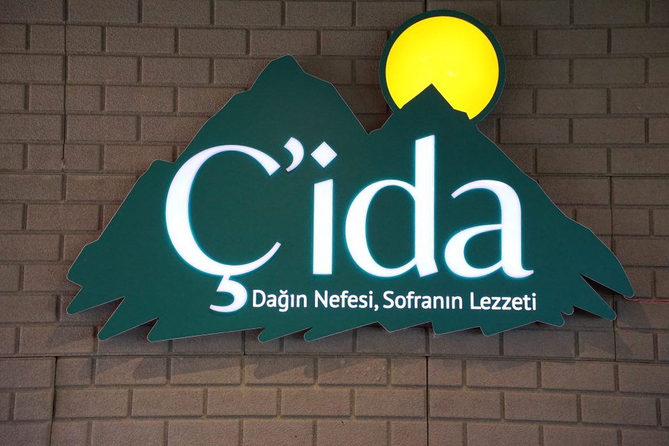 Duvara asılı Çida logosu: dağ silueti, güneş ve "Dağın Nefesi, Sofranın Lezzeti" yazısı